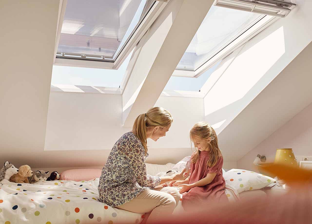 Midthengslet Velux takvindu med en mor og en datter som sitter på en seng foran