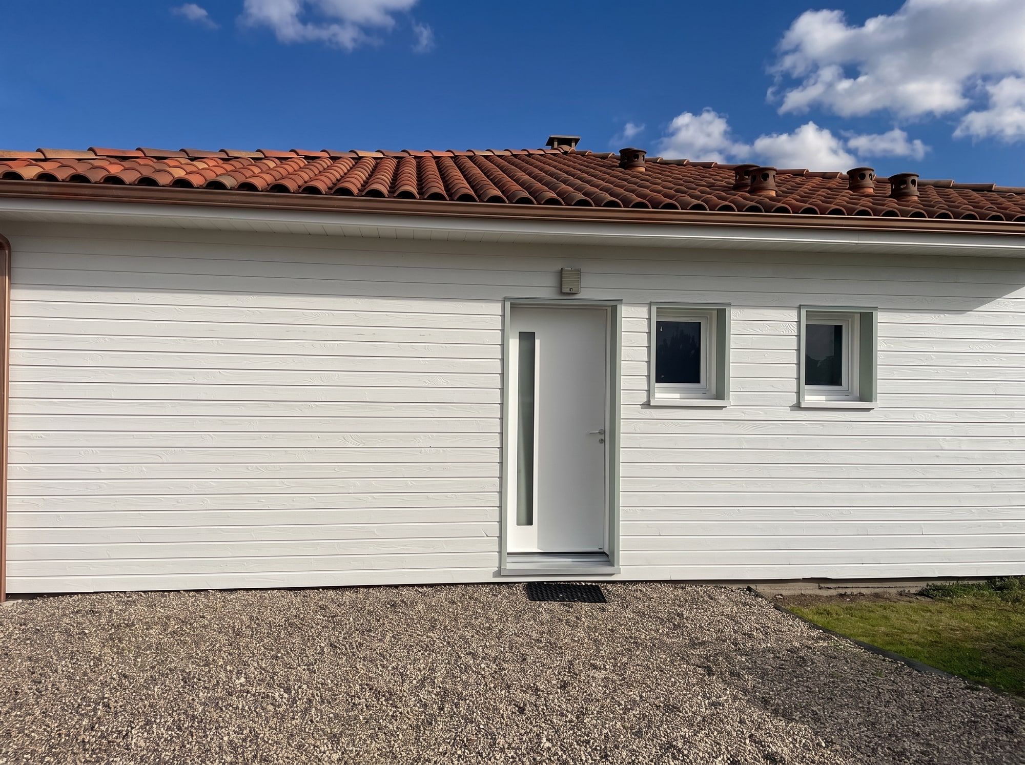 Entrée de la maison à ossature bois rénovée, bardage et menuiseries repeints en blanc cassé, Castelnau-sur-Gupie près de Marmande