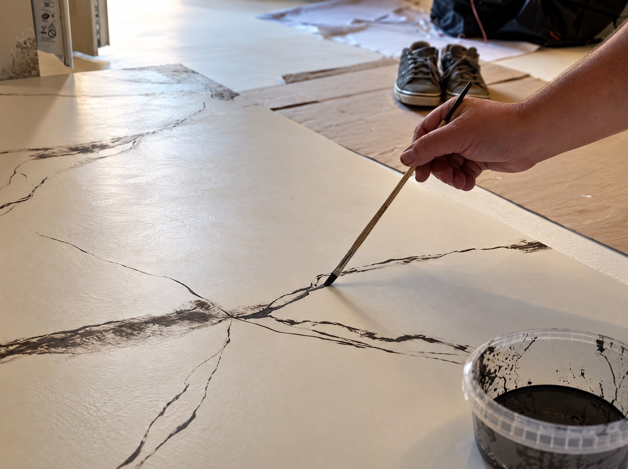 Veine de marbre tracée à la main à la baguette souple trempée dans le pigment, sur le micro-ciment blanc, Le Mas-d’Agenais (47)