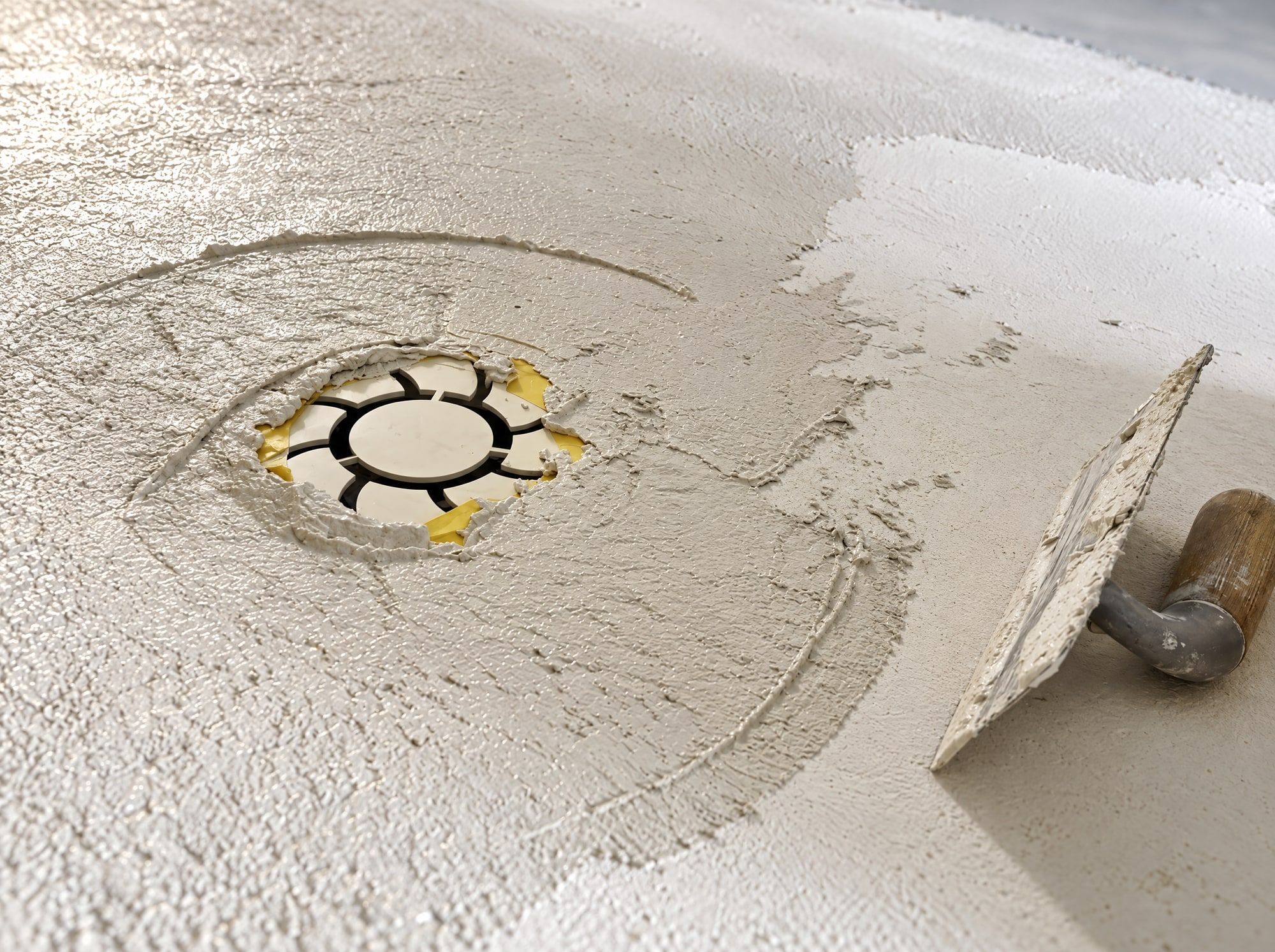 Béton ciré ramené à la main autour de la bonde de sol protégée, raccord d’évacuation au ras du revêtement, Le Mas-d’Agenais (47)