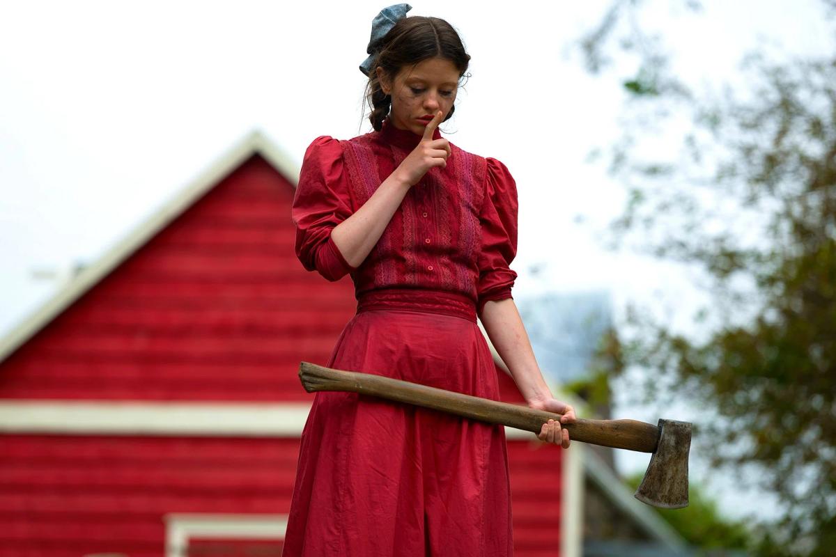 Pearl wearing a bright red dress while holding an axe outside the farmhouse
