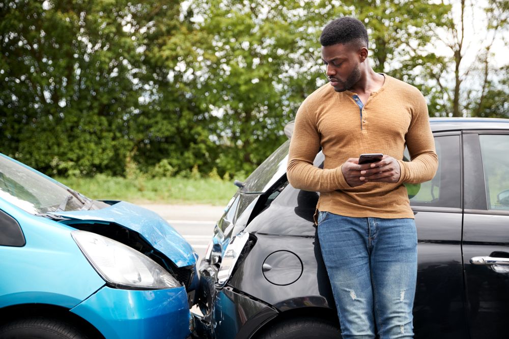 Man standing near two damaged cars after a low-speed car accident in Houston reviewing the scene on his phone