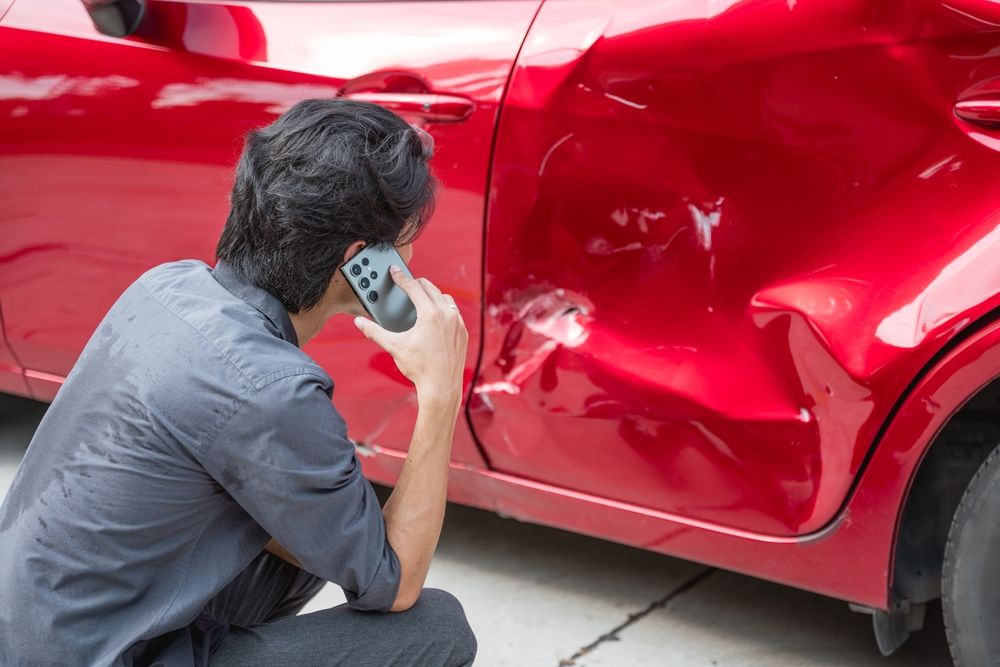 Driver on phone inspecting red car damage after a Texas T-bone accident at an intersection