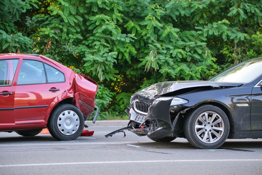 A red sedan with significant rear-end damage and a black sedan with a crushed front bumper following a motor vehicle accident on a Texas road.