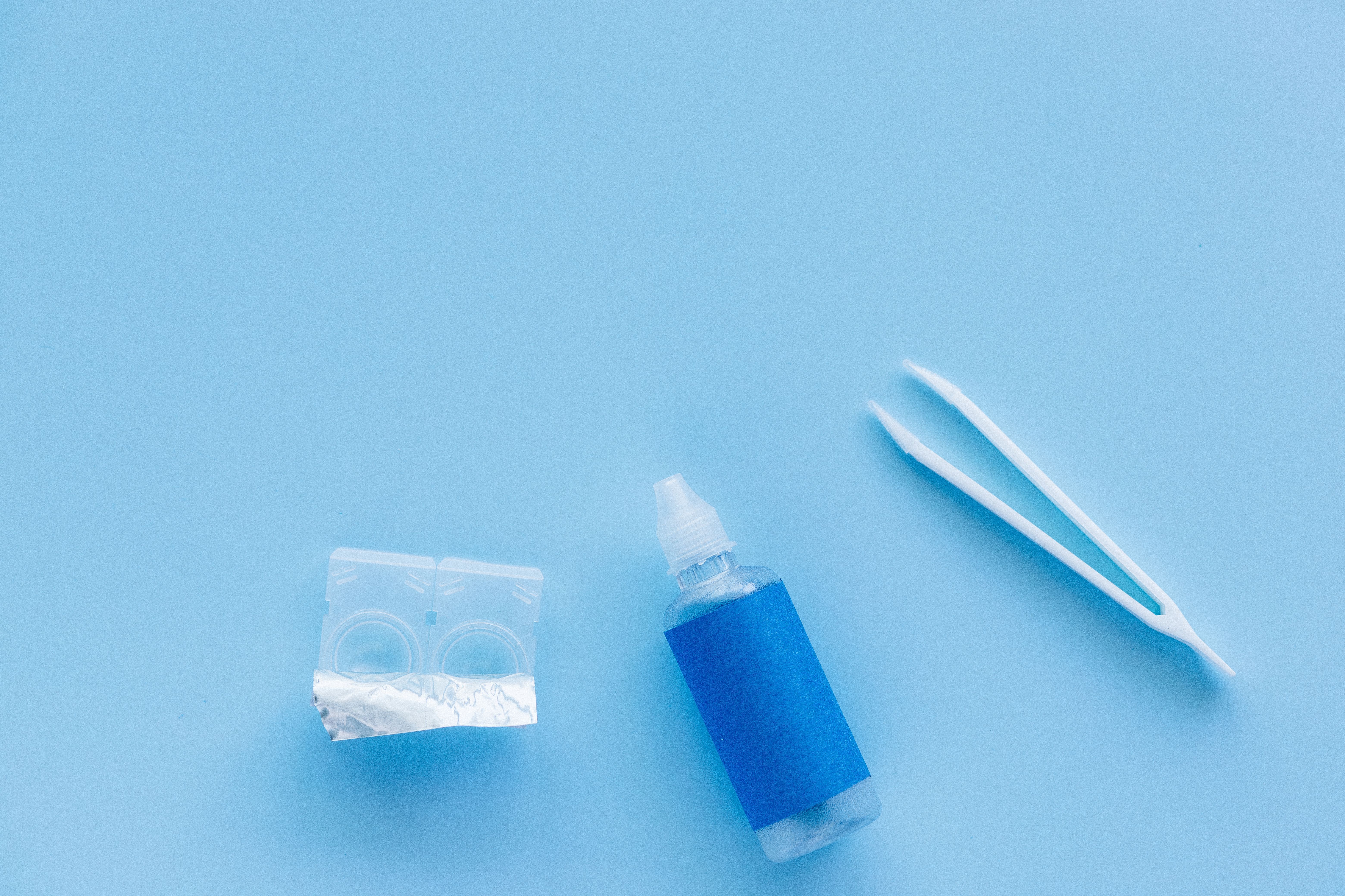 Estuche para lentes de contacto, botella de solución y pinzas sobre un fondo azul