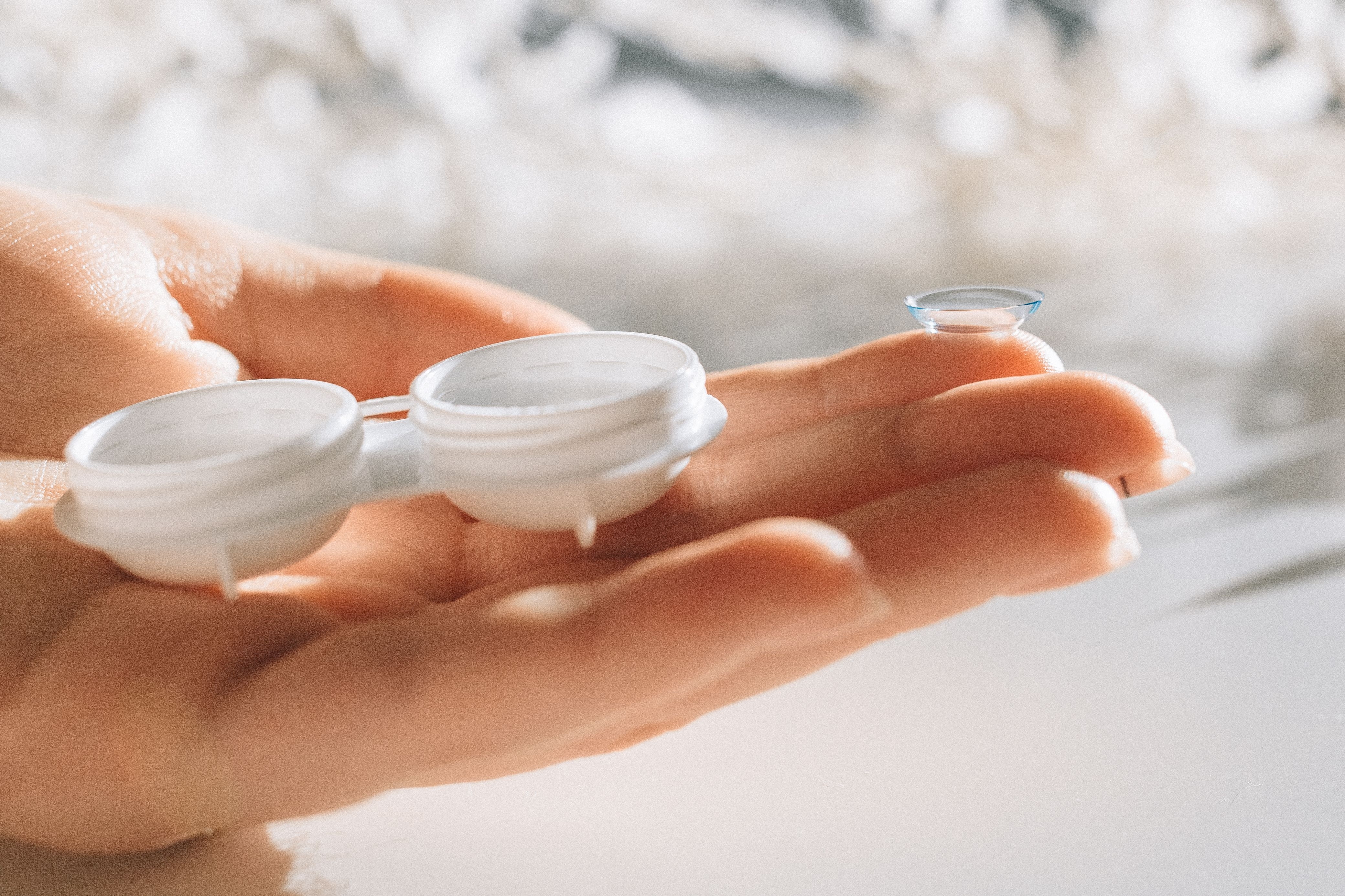 Image Hand holding a contact lens case and a single contact lens balanced on a fingertip.