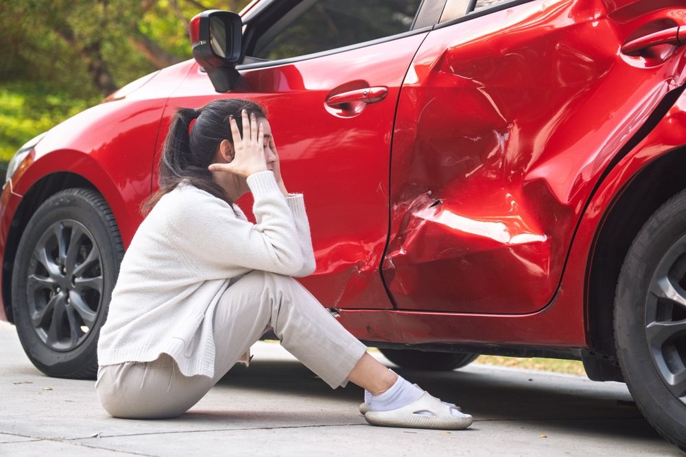 Injured driver sitting on the ground next to a damaged red car after a Houston Rodeo traffic accident near NRG Stadium