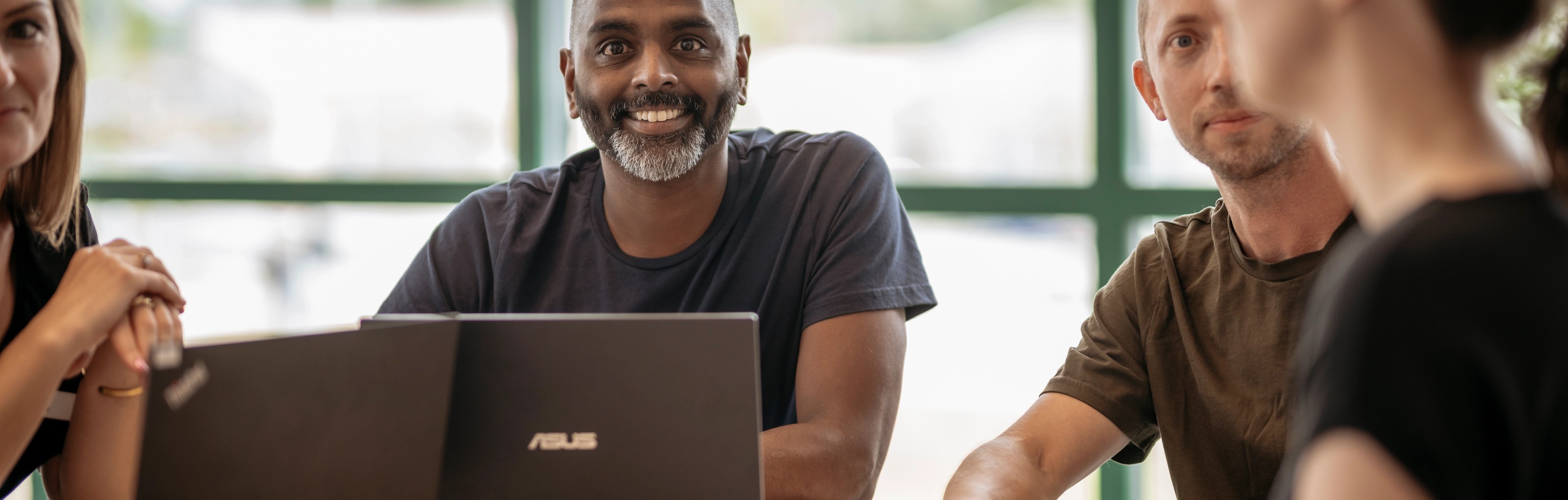 Glada lärare sitter tillsammans runt ett bord med datorer