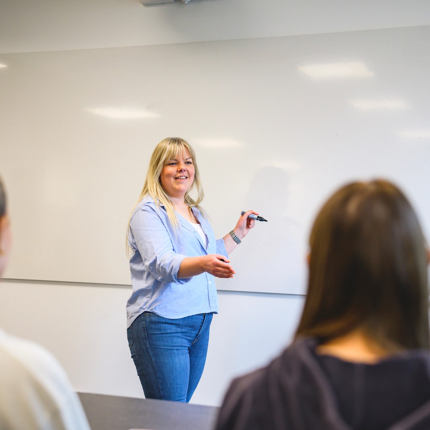 Lärare står vid whiteboard framför elever 