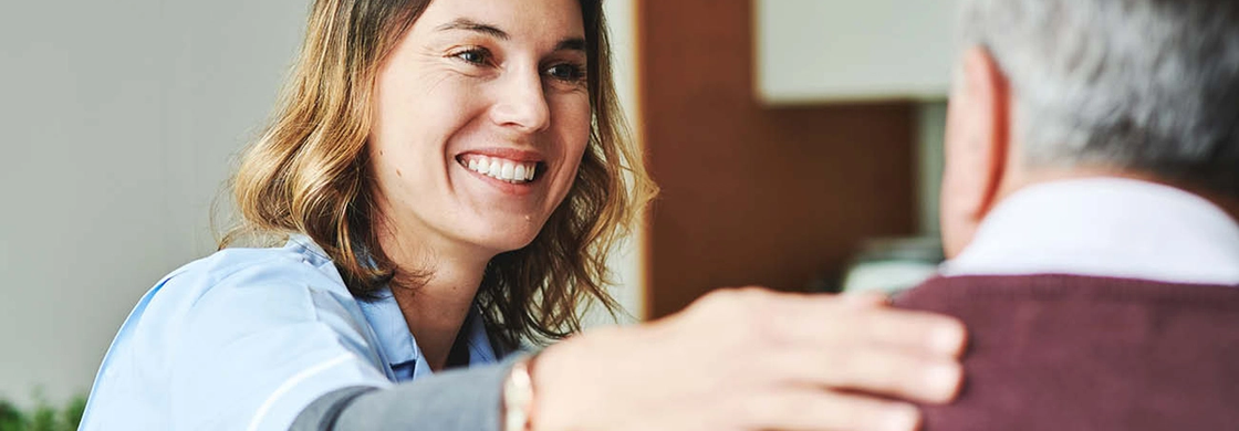 Kvinna i vårdkläder ler mot äldre man