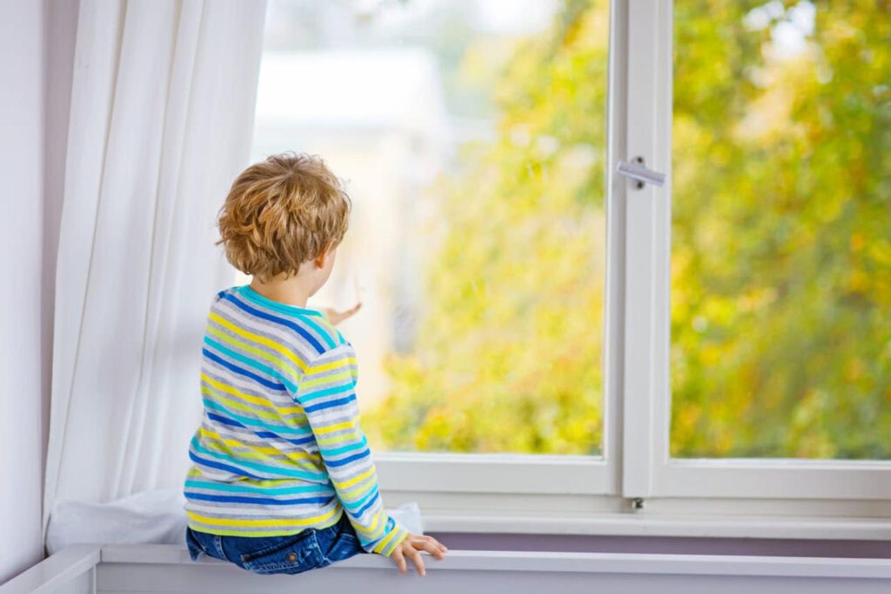 Child sitting near window and looking on autumn trees