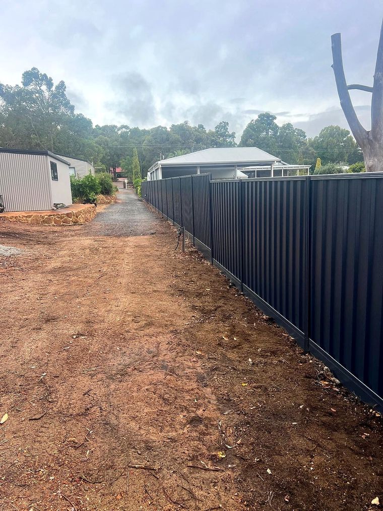 Charcoal Colorbond boundary fence along a gravel path beside freshly planted young trees in the Perth Hills