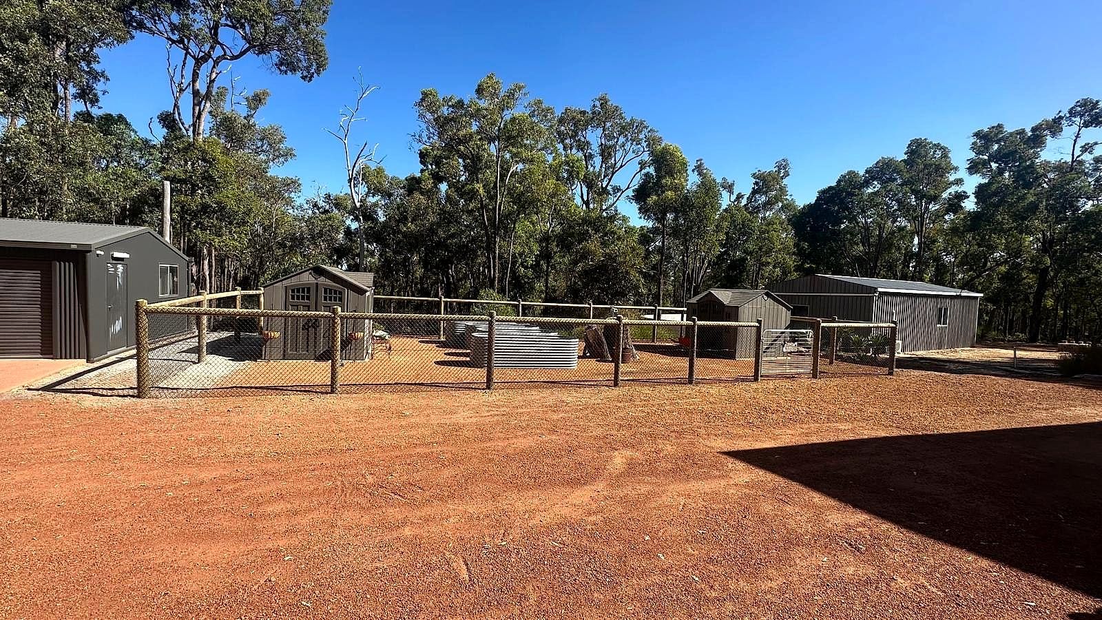 Rural fencing and stock-yard enclosures on a red-dirt bushland property in the Perth Hills