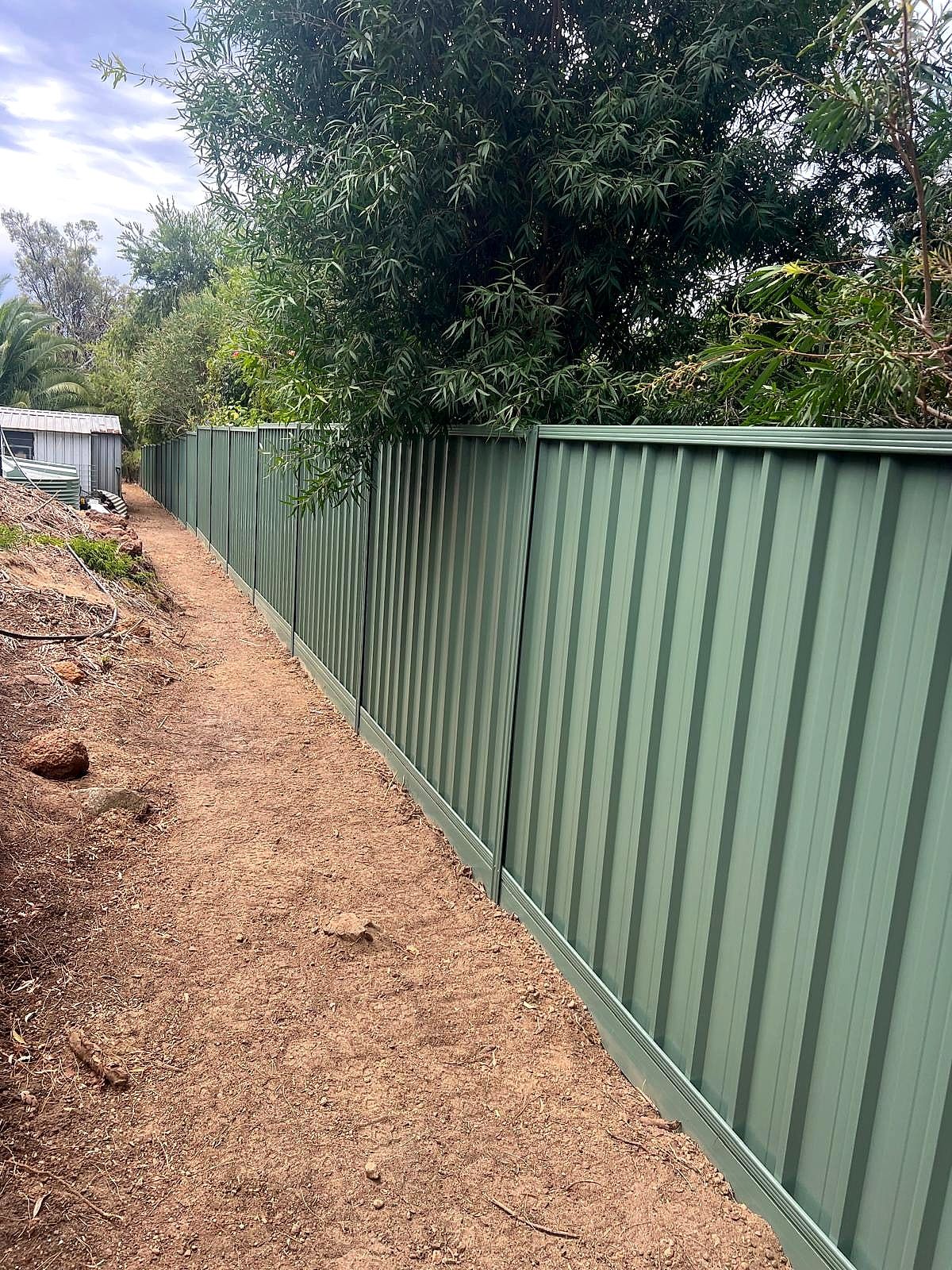 Green Colorbond fence running beside a red dirt track through native bushland in the Perth Hills