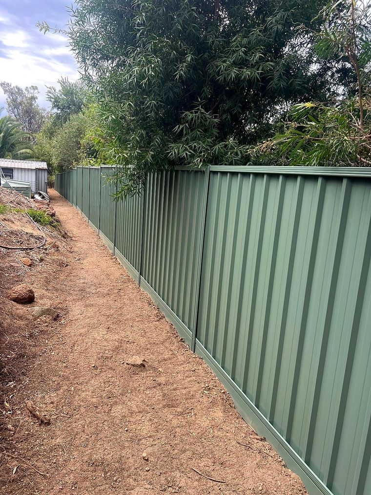 Green Colorbond fence running beside a red dirt track through native bushland in the Perth Hills