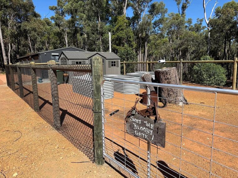 Galvanised mesh and tubular farm gate enclosing sheds and water tanks on a bushland Perth Hills property