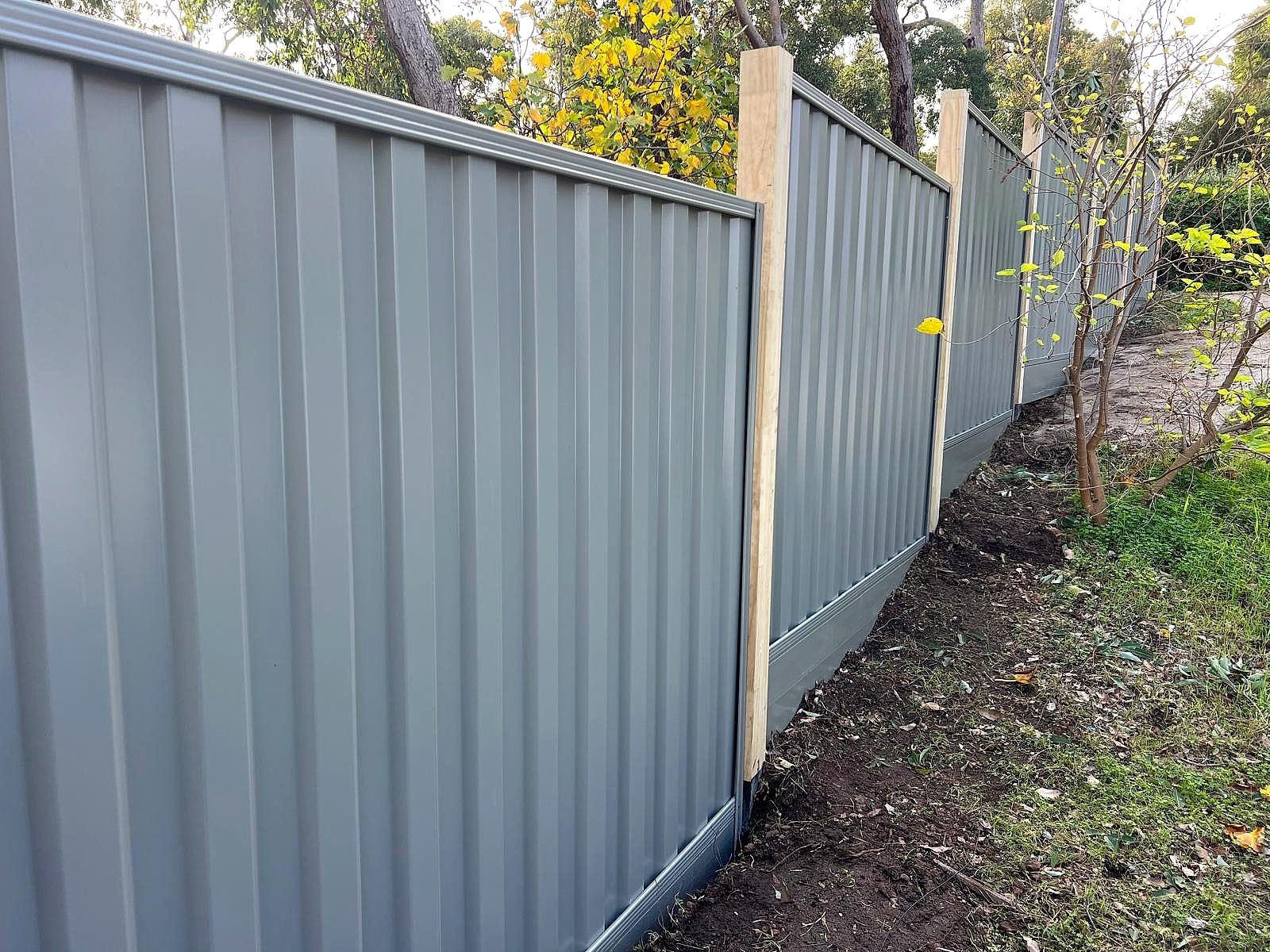 Grey Colorbond boundary fence with timber posts running through bushland with autumn-coloured leaves in the Perth Hills