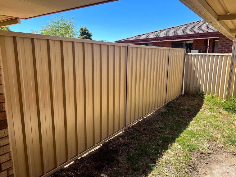 Cream Colorbond boundary fence beside a home with a green lawn in the Perth Hills