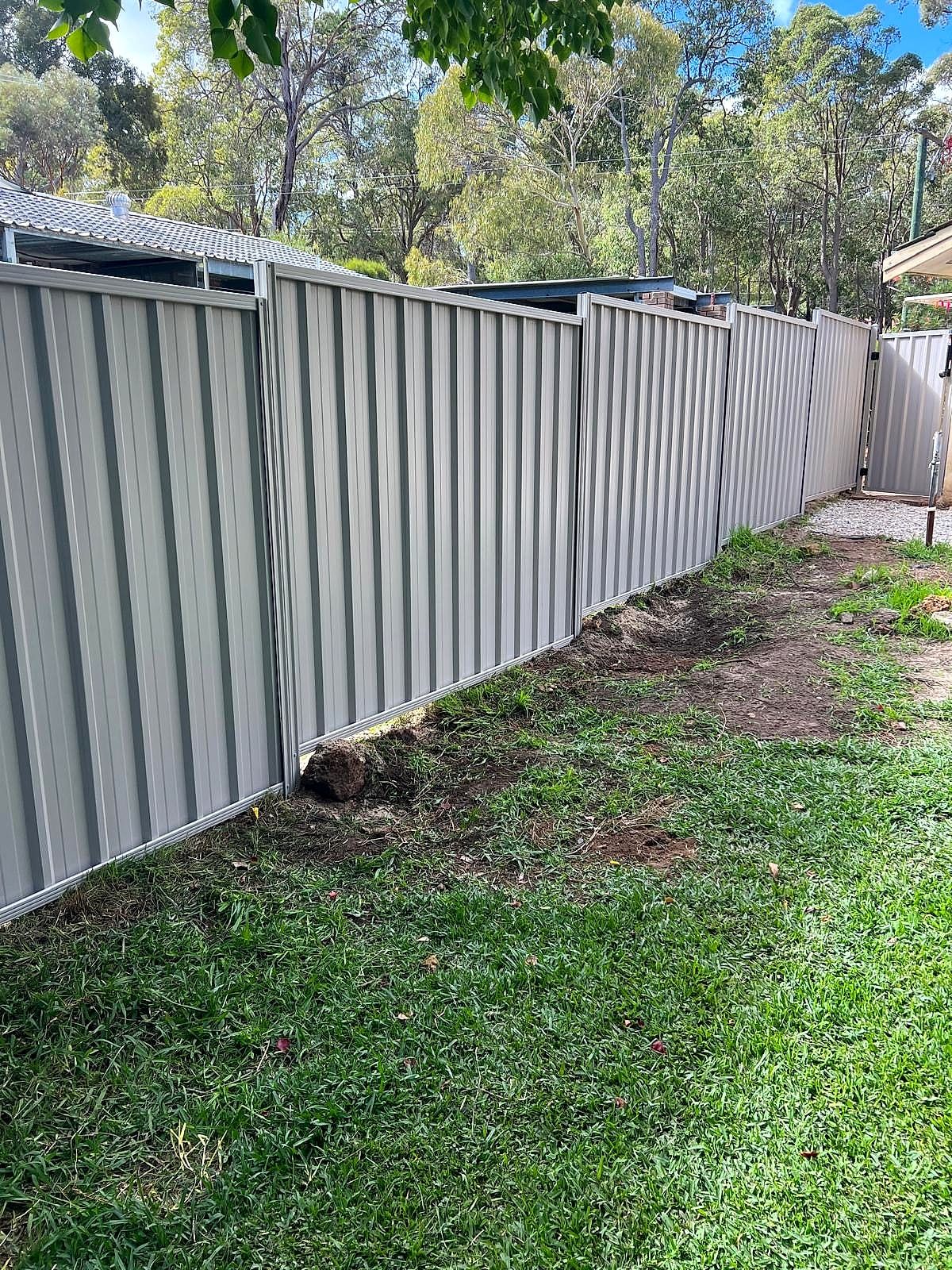 Grey Colorbond fence line running along a mowed lawn beside a tiled-roof home in the Perth Hills
