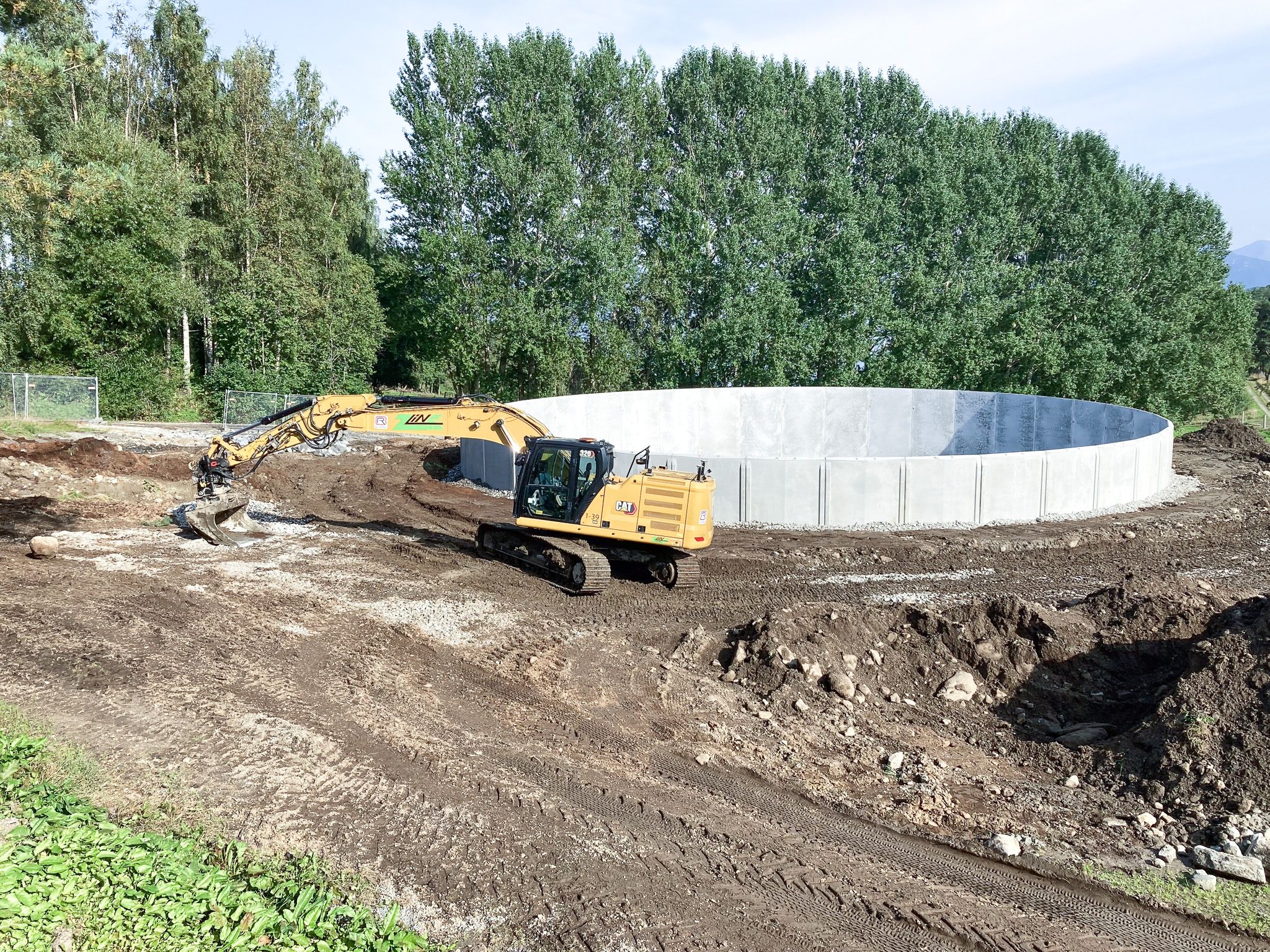 en byggeplass med elektrisk gravemaskin og en stor rund betongvegg