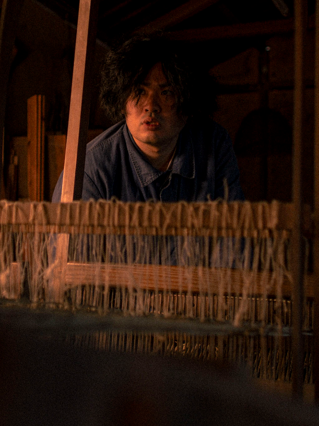 Ryuki Sunami standing behind a traditional loom in his igusa weaving workshop.