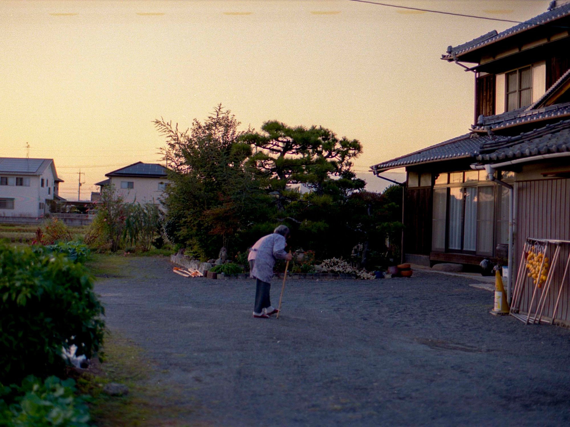A resident sweeping the grounds of a traditional Japanese home at dusk.