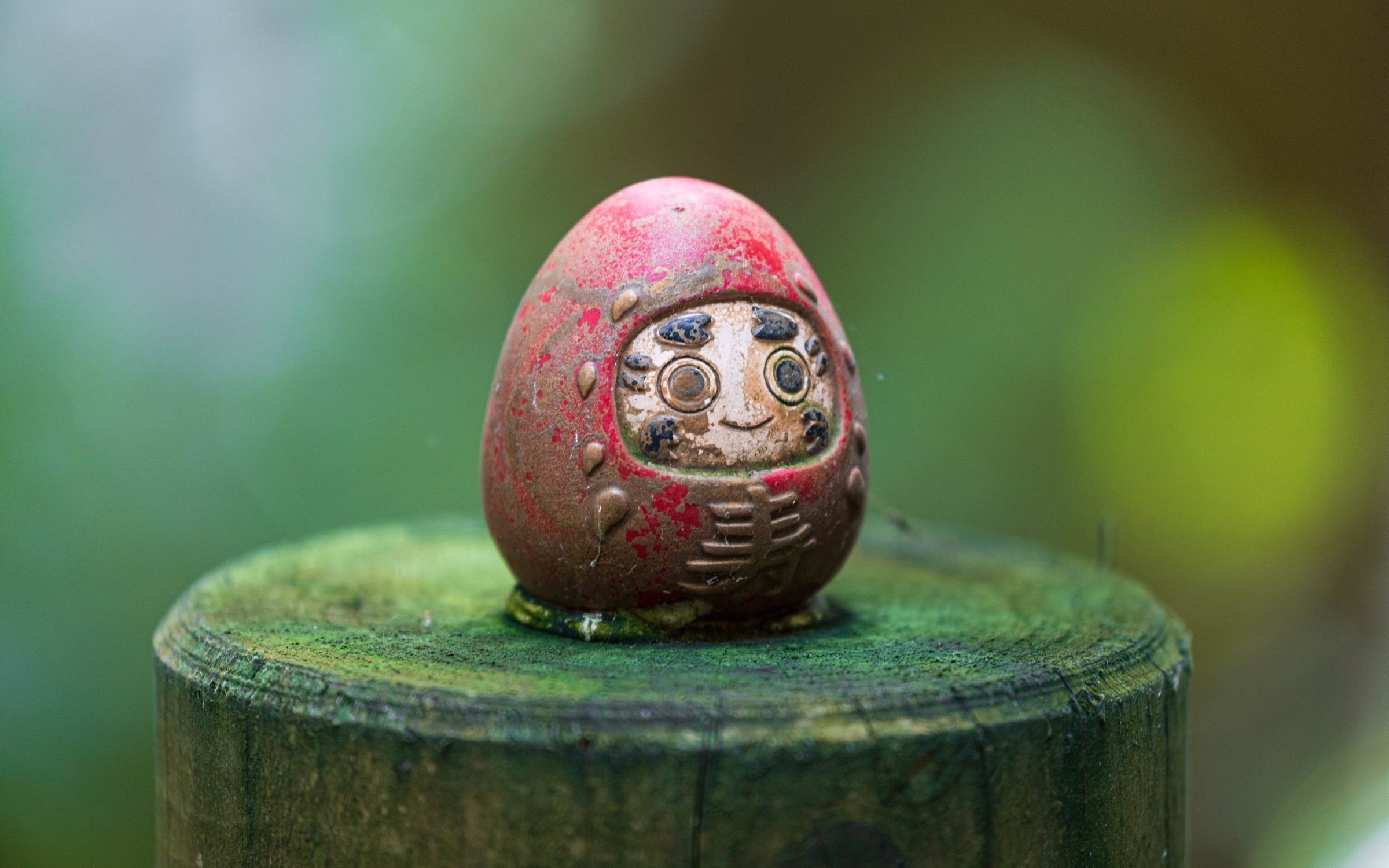 Détail d’un petit daruma patiné posé dans un environnement moussu.