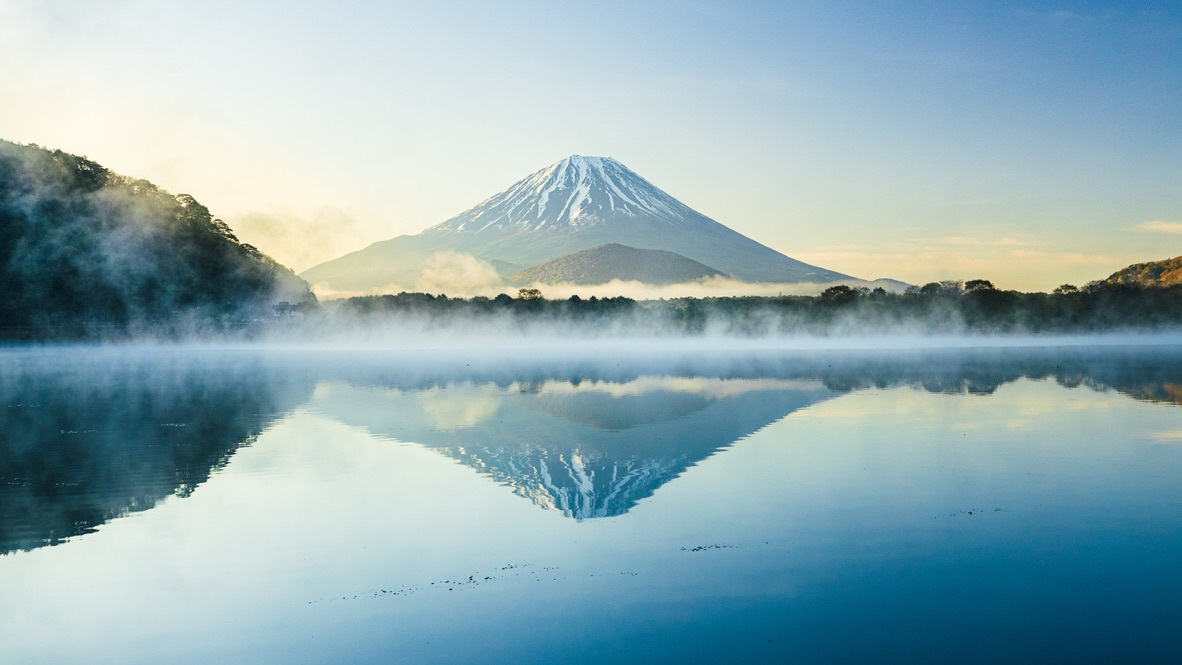 Le mont Fuji et son reflet apparaissent au-dessus d’une fine nappe de brume.