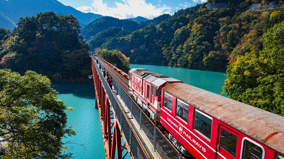 Un train rouge franchit un pont au-dessus des eaux turquoise d’une vallée de Shizuoka.