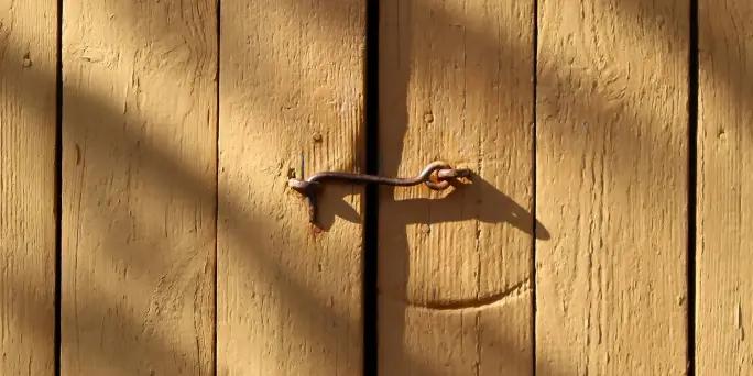 A metal hook-and-eye latch fastening a sunlit wooden door.