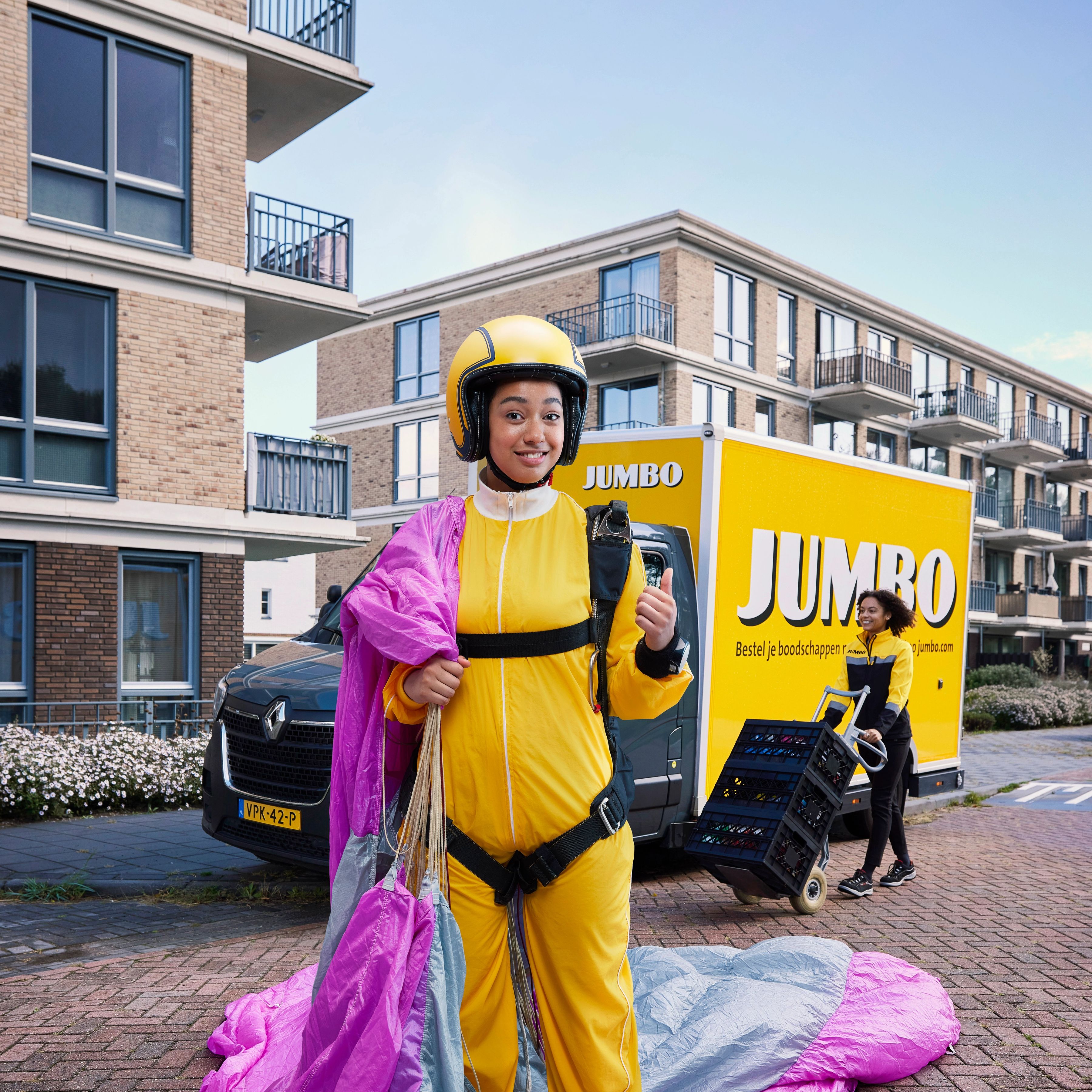 Meisje in geel parachutistenpak voor Jumbo bezorgbus