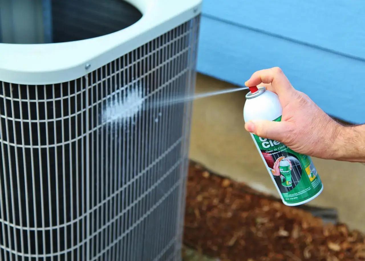 Hand spraying foam coil cleaner onto an outdoor air conditioning unit
