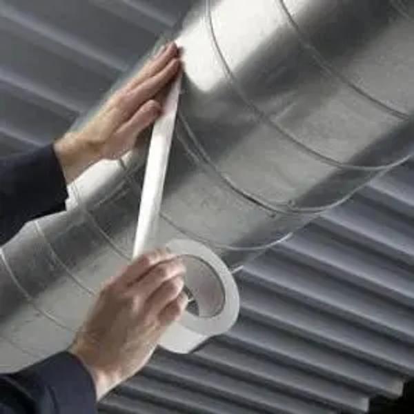 Hands sealing a joint in a round metal duct with foil tape