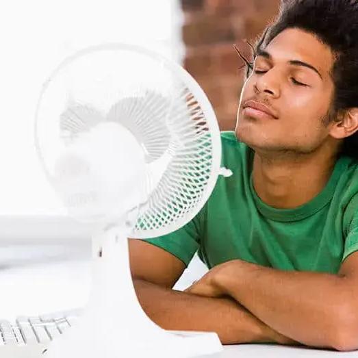 Young man at a desk enjoying the breeze from a small fan