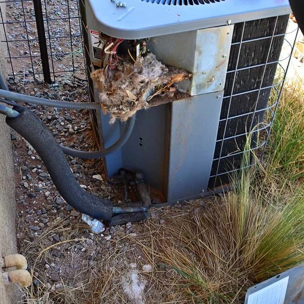 Outdoor air conditioning unit with a bird's nest and debris packed into its side