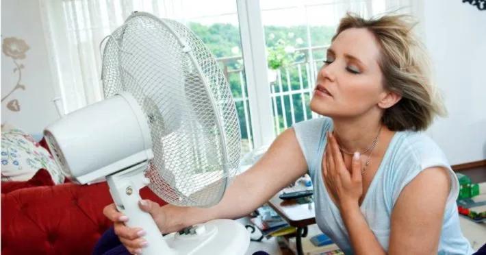Woman sitting in front of a desk fan, fanning her neck in the heat