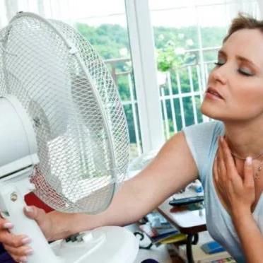 Woman sitting in front of a desk fan, fanning her neck in the heat