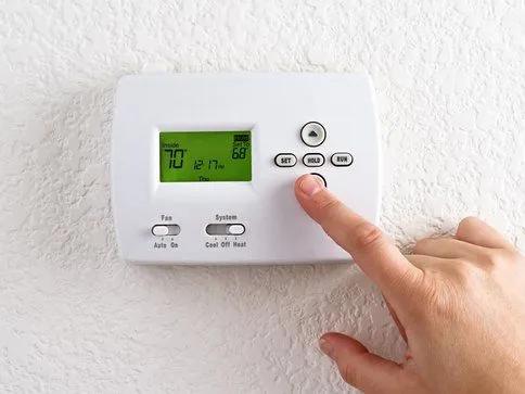 Finger pressing a button on a wall thermostat showing 70 degrees