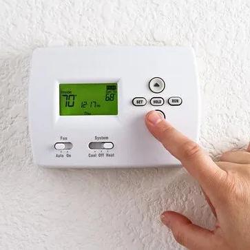 Finger pressing a button on a wall thermostat showing 70 degrees