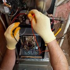 Gloved hands testing the wiring inside an open furnace with a multimeter