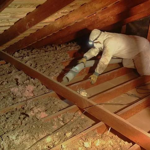 Worker crawling across the joists of a large attic