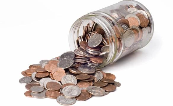Jar of coins tipped over and spilling onto a white surface