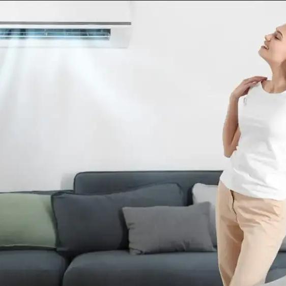 Woman relaxing on a couch beneath a wall-mounted ductless air conditioner