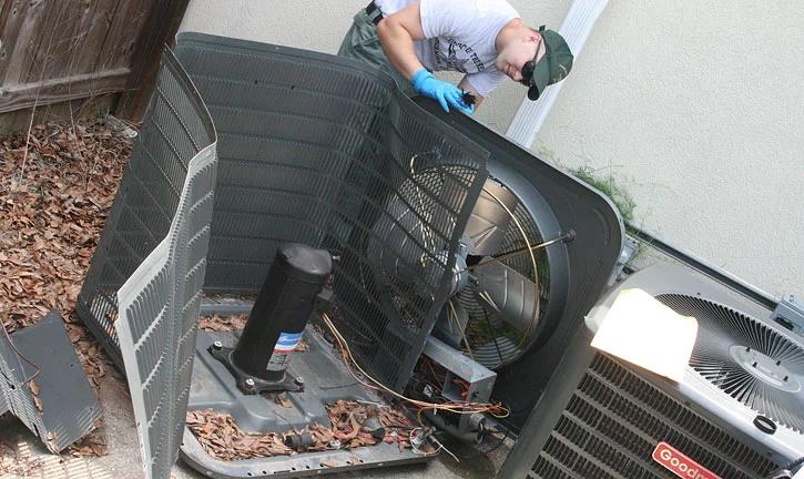 Technician working inside an outdoor air conditioning unit with its top panel removed