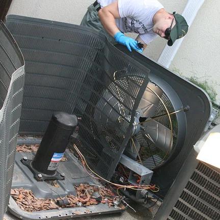 Technician working inside an outdoor air conditioning unit with its top panel removed