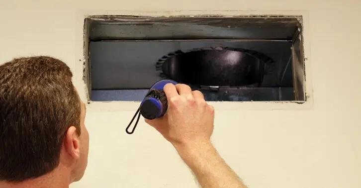 Man shining a flashlight into an open ceiling air duct