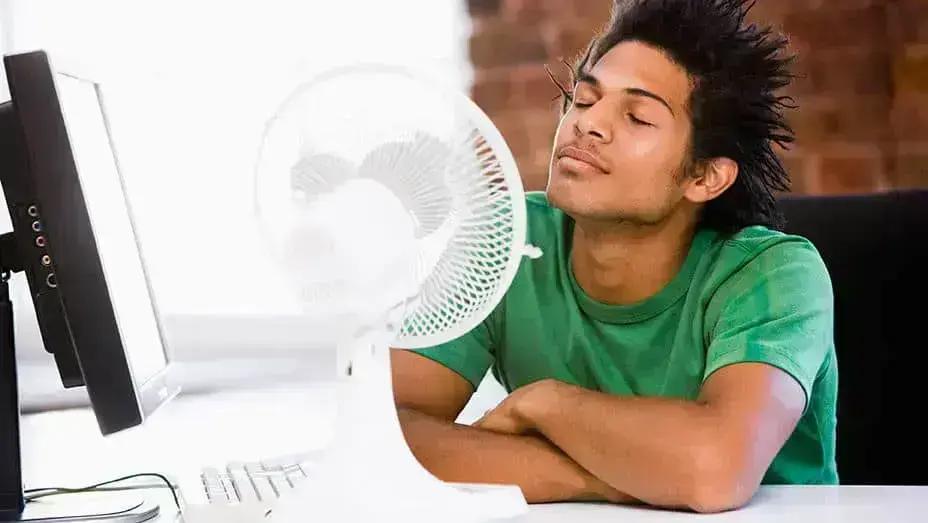 Young man at a desk enjoying the breeze from a small fan
