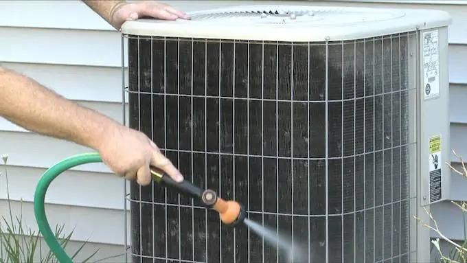 Spraying the fins of an outdoor air conditioning unit clean with a garden hose