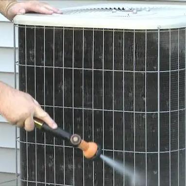 Spraying the fins of an outdoor air conditioning unit clean with a garden hose