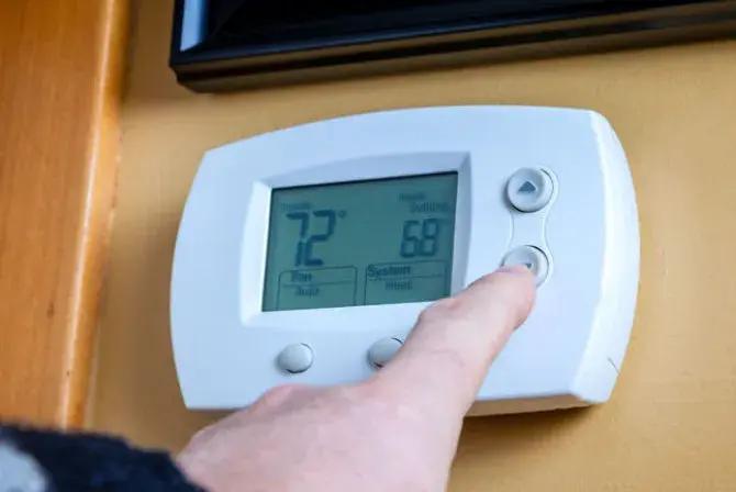 Finger pressing a button on a wall thermostat showing 72 degrees